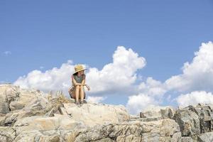 Woman sitting on the rocks in front of the ocean with clouds in the sky photo