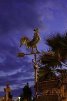 Metal weather vane with a rooster on the background of the evening sky photo