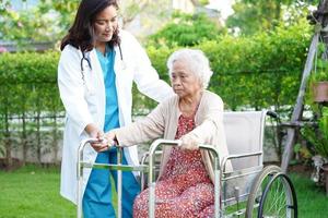 Doctor help Asian elderly woman disability patient walk with walker in nursing hospital, medical concept. photo