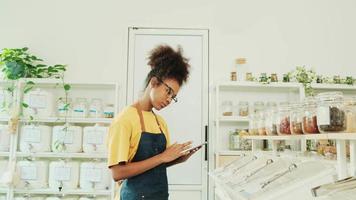Black female shopkeeper checks stock of natural organic products at retail display in refill store, zero-waste and plastic-free grocery shop, eco-friendly, sustainable lifestyles, reusable containers. video