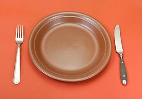 above view of ceramic plate, fork, knife on red photo