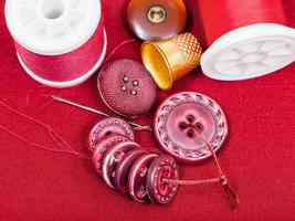 sewing thread, buttons, thimble on red textile photo