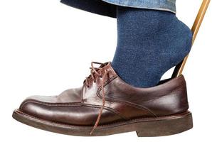 man puts on brown shoes using shoe horn isolated photo
