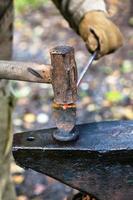 Blacksmith chops rod with sledgehammer and chisel photo