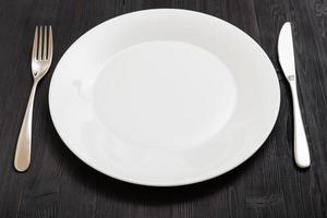 plato blanco con cuchillo, cuchara sobre mesa marrón oscuro foto