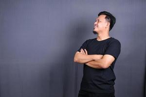 Smiling handsome asian man in black t-shirt standing with crossed arms isolated on gray background photo