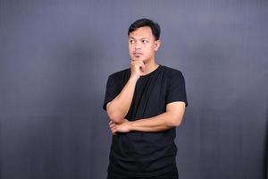 Asian young man thinking about things or idea wearing black t-shirt. Isolated gray background photo