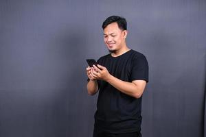 Photo of attractive asian guy holding mobile phone wear black t-shirt isolated gray color background