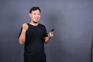 Happy Asian man holding a smartphone and winning the prize. isolated on gray background photo