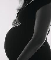 mujer adulta joven embarazada vestida de blanco tocando una gran barriga desnuda con las manos. mostrando forma. concepto de embarazo. tiempo de expectativa. de cerca. aislado sobre fondo de pared gris claro. foto