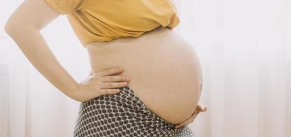 Young adult pregnant woman in white clothes touching big naked belly with hands. Showing shape. Pregnancy concept. Expectation time. Closeup. Isolated on light gray wall background. photo