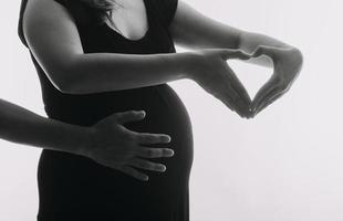 mujer adulta joven embarazada vestida de blanco tocando una gran barriga desnuda con las manos. mostrando forma. concepto de embarazo. tiempo de expectativa. de cerca. aislado sobre fondo de pared gris claro. foto