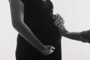 mujer adulta joven embarazada vestida de blanco tocando una gran barriga desnuda con las manos. mostrando forma. concepto de embarazo. tiempo de expectativa. de cerca. aislado sobre fondo de pared gris claro. foto