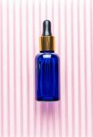 Blue glass dropper bottle with beauty care serum, hyaluronic acid and vitamins on pink background. Home cosmetics and spa concept photo