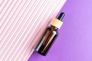 Amber glass cosmetic dropper bottle with blank label on double pink and purple background. Trendy beauty product design, branding. Mockup cosmetics photo