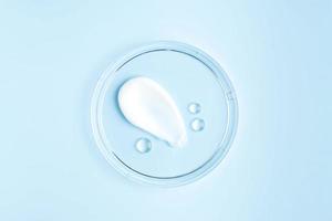 smear of cream stroke and round transparent drops of gel serum in a petri dish on a blue background. Concept laboratory tests and research, making and testing cosmetic photo