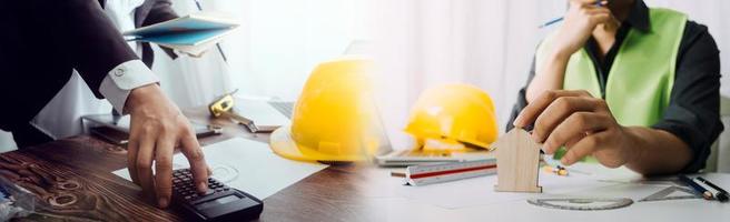 Two colleagues discussing data working and tablet, laptop with on on architectural project at construction site at desk in office photo