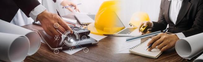Two colleagues discussing data working and tablet, laptop with on on architectural project at construction site at desk in office photo