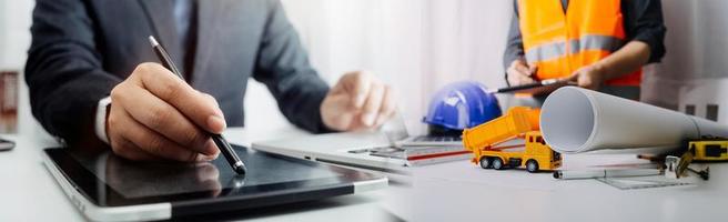 Two colleagues discussing data working and tablet, laptop with on on architectural project at construction site at desk in office photo