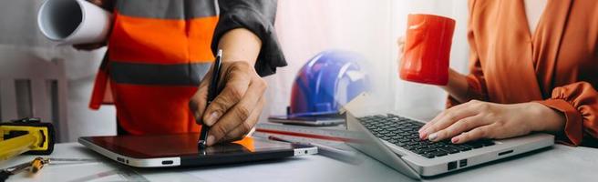 Two colleagues discussing data working and tablet, laptop with on on architectural project at construction site at desk in office photo