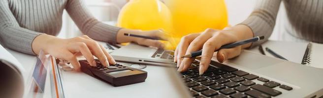 Two colleagues discussing data working and tablet, laptop with on on architectural project at construction site at desk in office photo