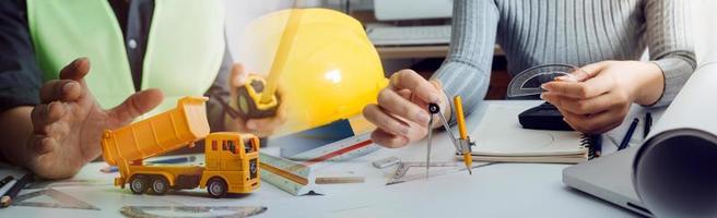 Two colleagues discussing data working and tablet, laptop with on on architectural project at construction site at desk in office photo