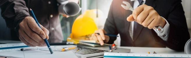 Two colleagues discussing data working and tablet, laptop with on on architectural project at construction site at desk in office photo