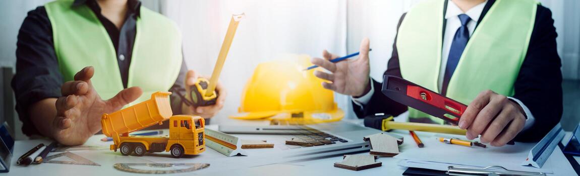 Two colleagues discussing data working and tablet, laptop with on on architectural project at construction site at desk in office photo
