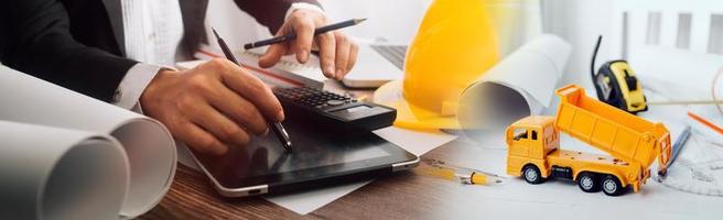 Two colleagues discussing data working and tablet, laptop with on on architectural project at construction site at desk in office photo