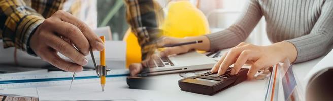 Two colleagues discussing data working and tablet, laptop with on on architectural project at construction site at desk in office photo