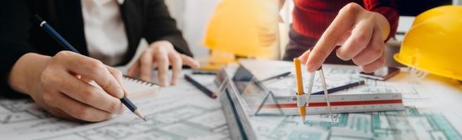 Two colleagues discussing data working and tablet, laptop with on on architectural project at construction site at desk in office photo