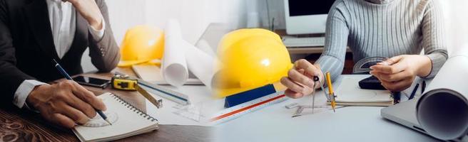 Two colleagues discussing data working and tablet, laptop with on on architectural project at construction site at desk in office photo