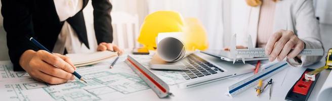 Two colleagues discussing data working and tablet, laptop with on on architectural project at construction site at desk in office photo