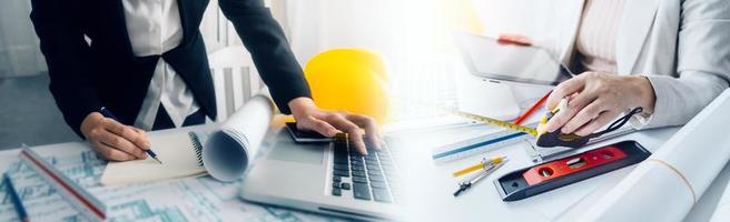 Two colleagues discussing data working and tablet, laptop with on on architectural project at construction site at desk in office photo