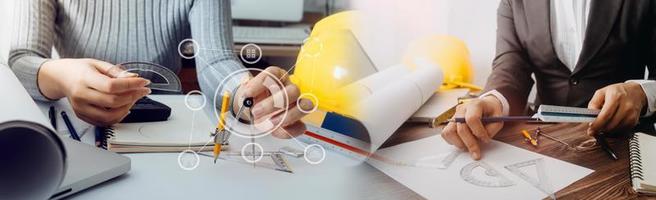 Two colleagues discussing data working and tablet, laptop with on on architectural project at construction site at desk in office photo