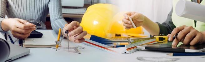 Two colleagues discussing data working and tablet, laptop with on on architectural project at construction site at desk in office photo