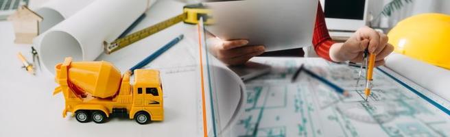 Two colleagues discussing data working and tablet, laptop with on on architectural project at construction site at desk in office photo