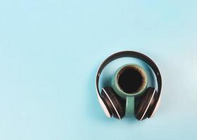 flat lay of blue cup of black coffee covered around with headphones on blue background. Music and coffee relaxing time concept. photo