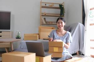 SME entrepreneur Small business entrepreneurs Online selling ideas,Happy Young Asian business owner work on computer and a boxs at home,delivery SME procurement package box deliver to customers, photo
