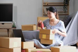 Small business entrepreneur SME, asian young woman,girl owner packing product, checking parcel for delivery to customer, using scotch tape to seal the box, working at home. Merchant online e commerce photo