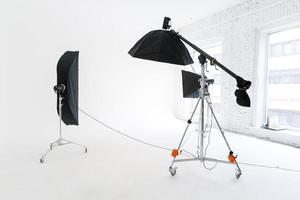 Empty photo studio with lighting equipment. Photographer workplace interior with professional tool set gear. Flash light white background scenes ready for studio shooting. Modern photographer studio