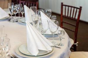 Fancy table set for dinner with napkin glasses in restaurant, luxury interior background. Wedding elegant banquet decoration and items for food arranged by catering service on white tablecloth table. photo