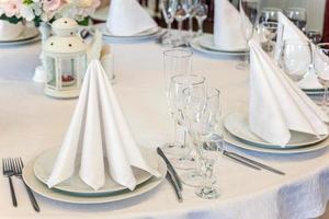 mesa elegante para cenar con vasos de servilleta en el restaurante, fondo interior de lujo. boda elegante decoración de banquetes y artículos para comida organizados por servicio de catering en mesa de mantel blanco. foto