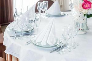 mesa elegante para cenar con vasos de servilleta en el restaurante, fondo interior de lujo. boda elegante decoración de banquetes y artículos para comida organizados por servicio de catering en mesa de mantel blanco. foto