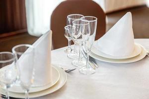 Fancy table set for dinner with napkin glasses in restaurant, luxury interior background. Wedding elegant banquet decoration and items for food arranged by catering service on white tablecloth table. photo