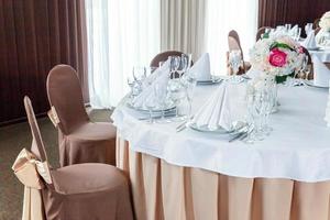 mesa elegante para cenar con composición floral en el restaurante, fondo interior de lujo. boda elegante decoración de banquetes y artículos para comida organizados por servicio de catering en mesa blanca. foto