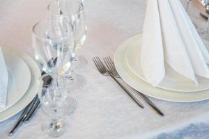 mesa elegante para cenar con vasos de servilleta en el restaurante, fondo interior de lujo. boda elegante decoración de banquetes y artículos para comida organizados por servicio de catering en mesa de mantel blanco. foto