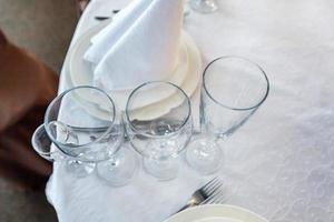 mesa elegante para cenar con vasos de servilleta en el restaurante, fondo interior de lujo. boda elegante decoración de banquetes y artículos para comida organizados por servicio de catering en mesa de mantel blanco. foto