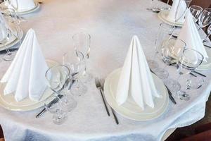 Fancy table set for dinner with napkin glasses in restaurant, luxury interior background. Wedding elegant banquet decoration and items for food arranged by catering service on white tablecloth table. photo