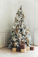 Classic christmas New Year decorated interior room New year tree. Christmas tree with gold decorations and gift boxes. Modern white classical style interior design apartment. Christmas eve at home. photo
